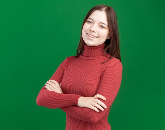 Smiling young pretty woman standing with closed posture looking at front isolated on green wall with copy space