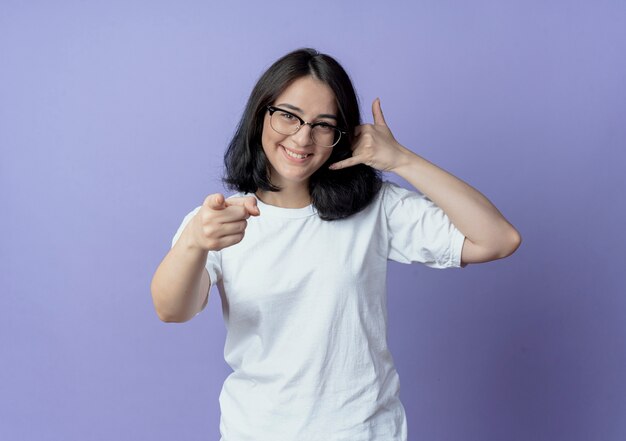 smiling young pretty woman wearing glasses doing call gesture and pointing at front