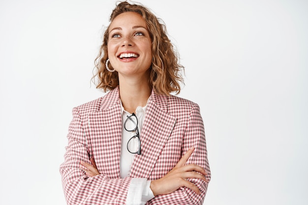 Free photo smiling young professional, businesswoman looking at upper left corner with hopeful face expression, standing on white.