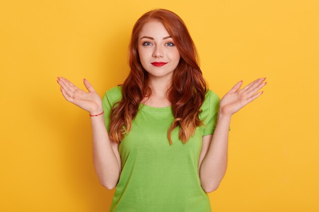 Smiling young red woman in casual clothes posing isolated, female spreading hands aside
