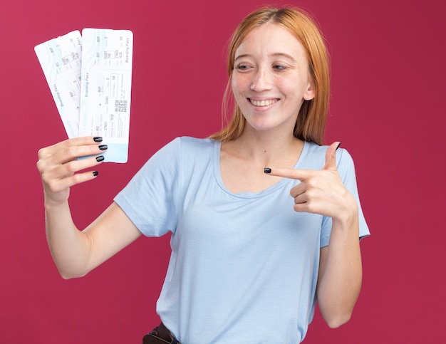 Smiling young redhead ginger girl with freckles holding and pointing at air tickets