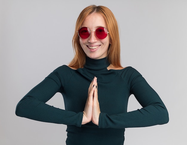 Smiling young redhead ginger girl with freckles in sun glasses holding hands together on white