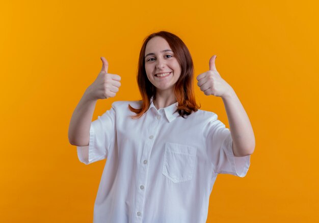 Smiling young redhead girl her thumbs up isolated on yellow wall