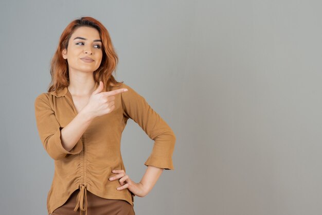 Smiling young redhead holding her finger up and looking away on grey wall