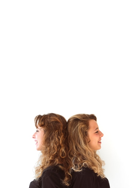 Smiling young sister standing back to back against white backdrop