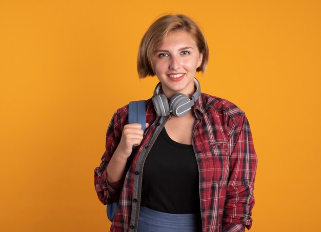 Smiling young slavic student girl with headphones wearing backpack looks at camera 