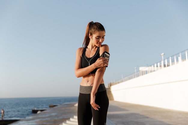 Smiling young sports woman listening music using mobile phone.