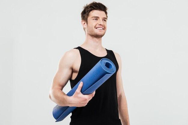 Smiling young sportsman holding fitness rug