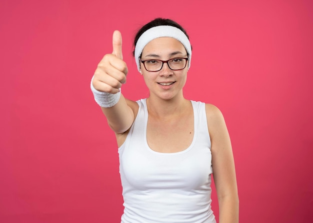 Улыбающаяся молодая спортивная девушка в оптических очках с повязкой на голову