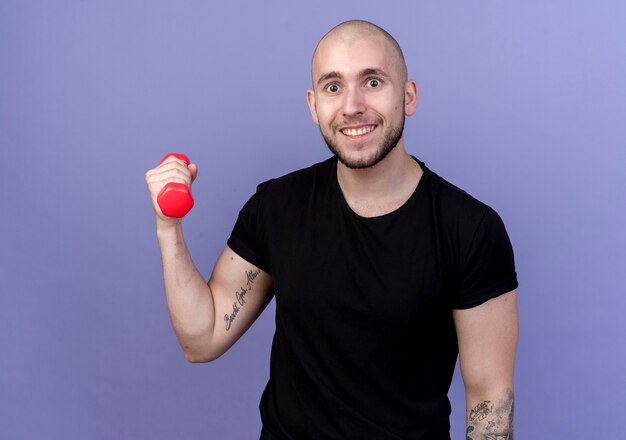 Smiling young sporty man holding dumbbell isolated on purple