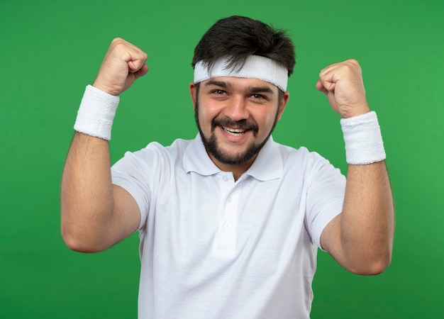 Smiling young sporty man wearing headband and wristband showing yes gesture