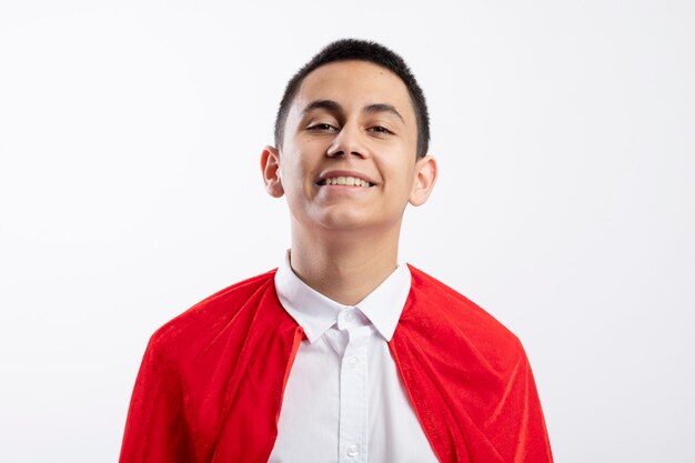 Smiling young superhero boy in red cape looking at camera isolated on white background