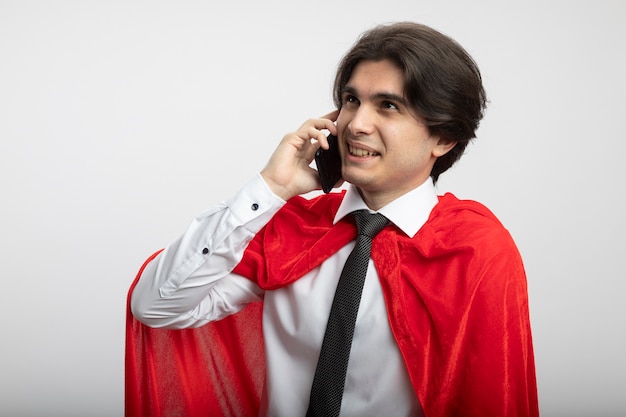 Улыбающийся молодой супергерой, смотрящий в сторону в галстуке, разговаривает по телефону на белом фоне
