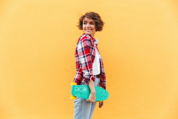 Foto gratuita giovane skateboard sorridente della tenuta dell'adolescente