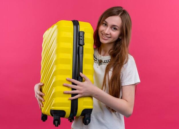Улыбающаяся молодая путешественница девушка держит чемодан на изолированной розовой стене