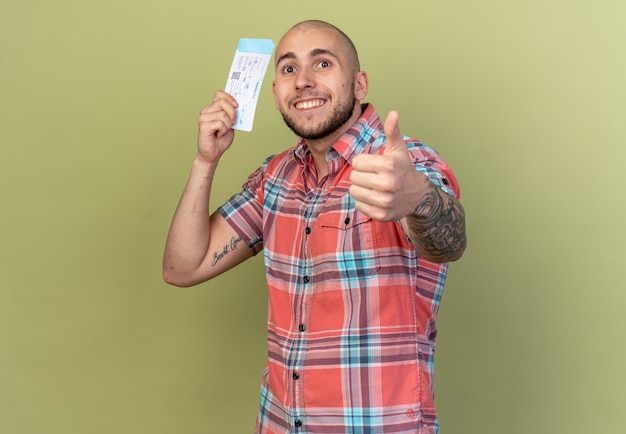 Free photo smiling young traveler man holding air tickets and thumbing up isolated on olive green wall with copy space