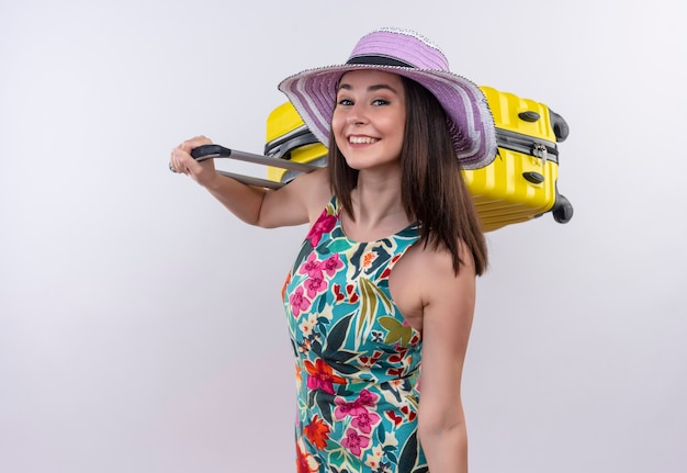 Smiling young traveler woman holding suitcase on isolated white wall