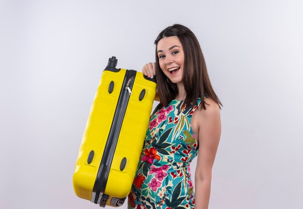 Улыбающаяся молодая путешественница в разноцветном платье держит мобильную сумку на белой стене