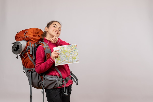 smiling young traveller with big backpack holding map on grey
