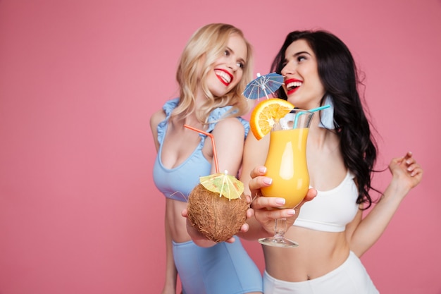 Smiling young two women dressed in swimwear drinking cocktails