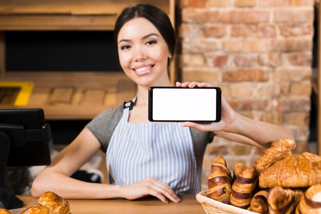 Smiling young woman at the bakery counter showing his mobile phone