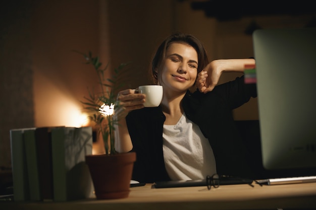 Smiling young woman designer stretching indoors at night