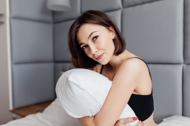 Бесплатное фото Улыбается молодая женщина, обнимая ее подушку утром в своей спальне у себя дома