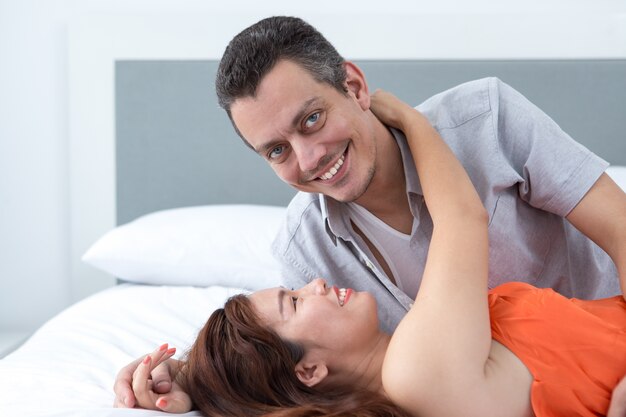 Улыбаясь молодая женщина, обнимая мужа в постели