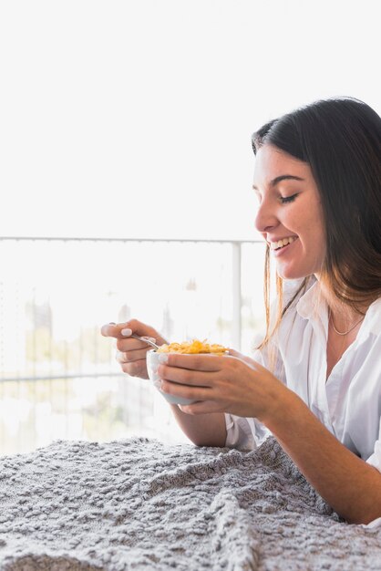 コーンフレークの朝食を楽しんでいる若い女性の笑みを浮かべてください。