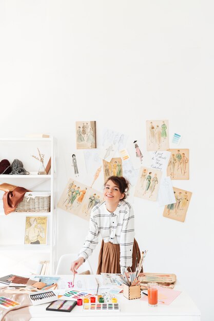 Smiling young woman fashion designer standing at her workplace
