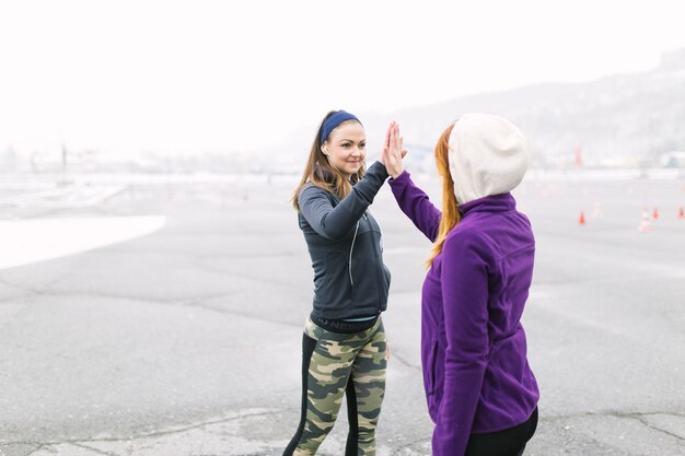 Smiling young woman giving high five to her friend at outdoors