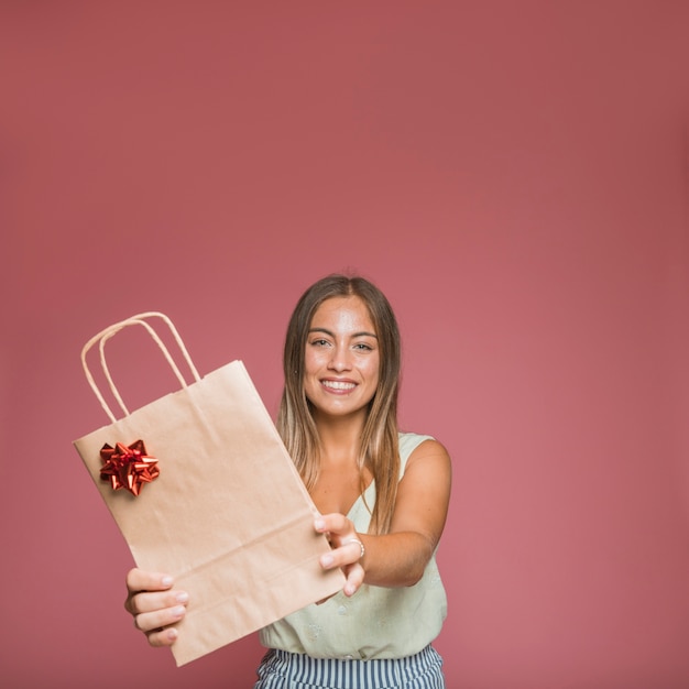 Smiling young woman giving paper shopping bag with red bow