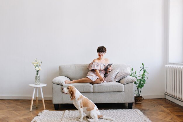Улыбающаяся молодая женщина в очках смотрит с улыбкой на собаку породы бигль, сидящую на ковре рядом с диваном