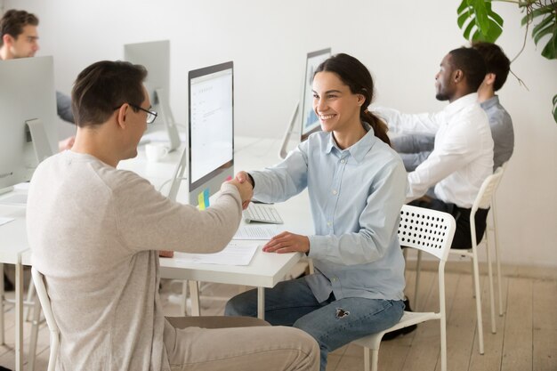 Smiling young woman handshaking satisfied client making deal in office