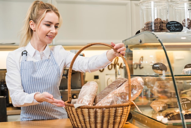 Smiling young woman holding basket of baguette in the coffee shop