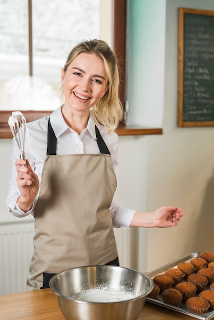 コーヒーショップで泡立て器でクリームを保持している若い女性を笑顔