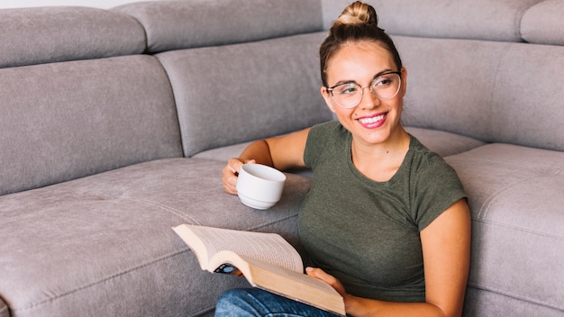 Smiling young woman holding cup of coffee and books looking away