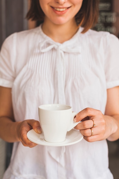 Smiling young woman holding cup of tasty coffee