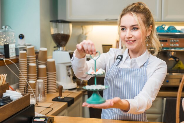 コーヒーショップでトレイを3層にメレンゲと砂糖の立方体を保持している若い女性の笑みを浮かべてください。