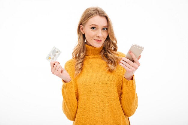 Улыбающиеся молодая женщина, держащая мобильный телефон и кредитную карту.