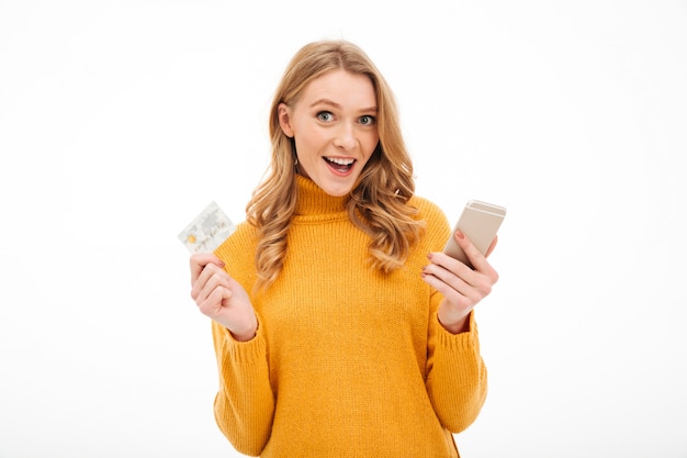 Smiling young woman holding mobile phone and credit card.