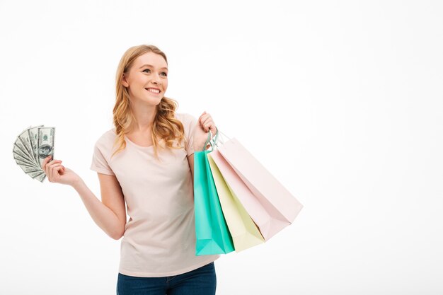 Smiling young woman holding money and shopping bags.