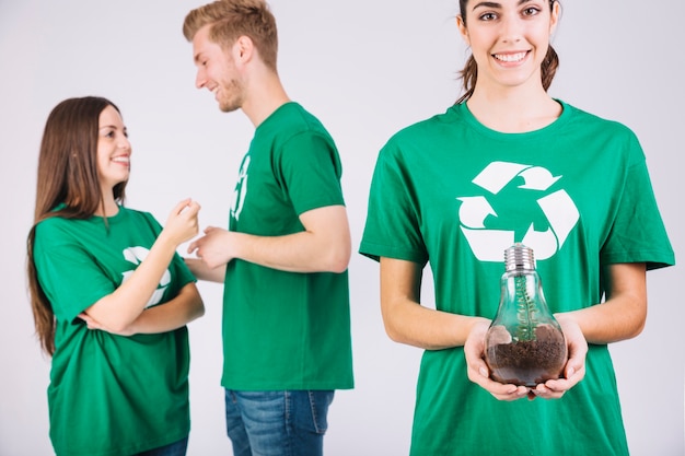 Smiling young woman holding sapling in light bulb