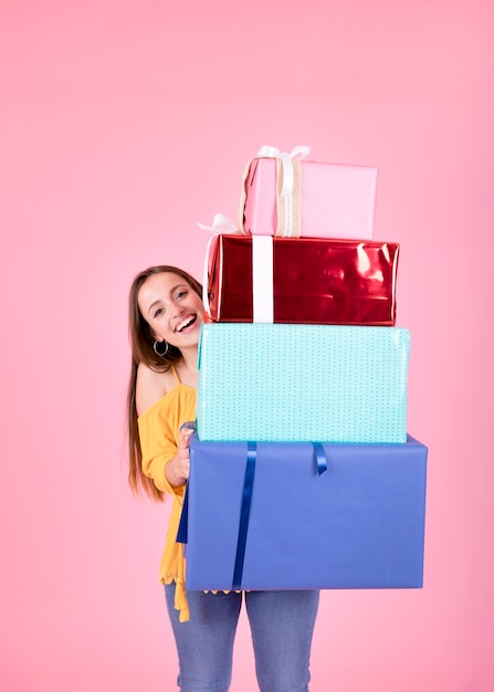 Pila sorridente della tenuta della giovane donna di contenitori di regalo che stanno contro il fondo rosa