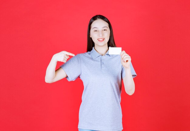 Smiling young woman holding visit card and point finger herself