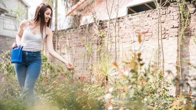 Free photo smiling young woman holding watering can in hand taking care of plants in the garden