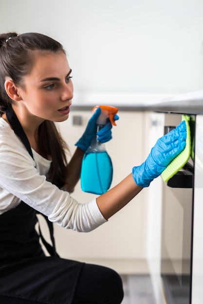 Smiling young woman housewife cleaning furniture in kitchen