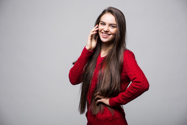 Smiling young woman is pointing on smartphone standing on white wall.