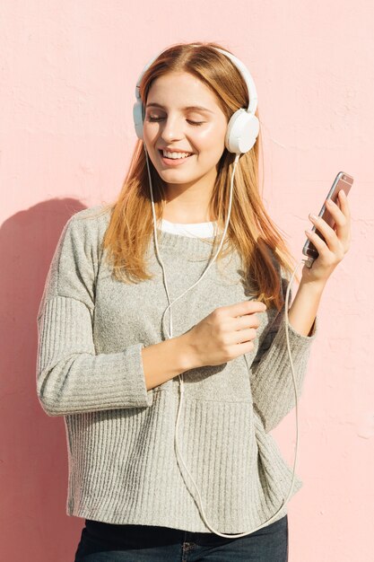 Smiling young woman listening music on headphone through mobile phone