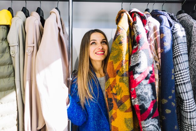 Smiling young woman looking at coats hanging on a rack